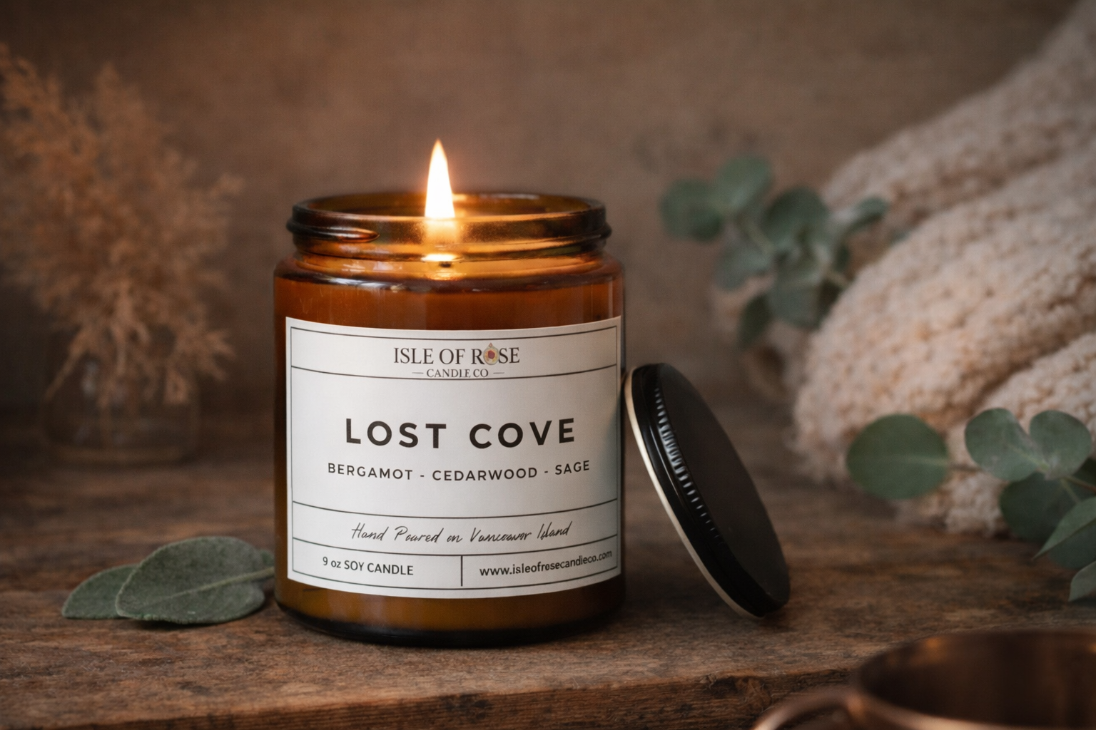 Candle labeled 'Lost Cove' by Isle of Rose on a wooden surface with eucalyptus leaves.
