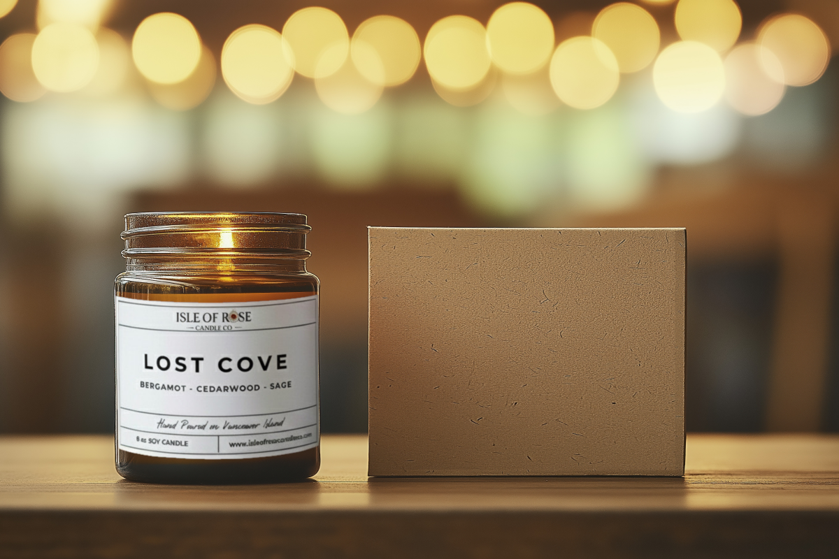 Candle jar labeled 'Lost Cove' with a cardboard box on a wooden surface, blurred lights in the background