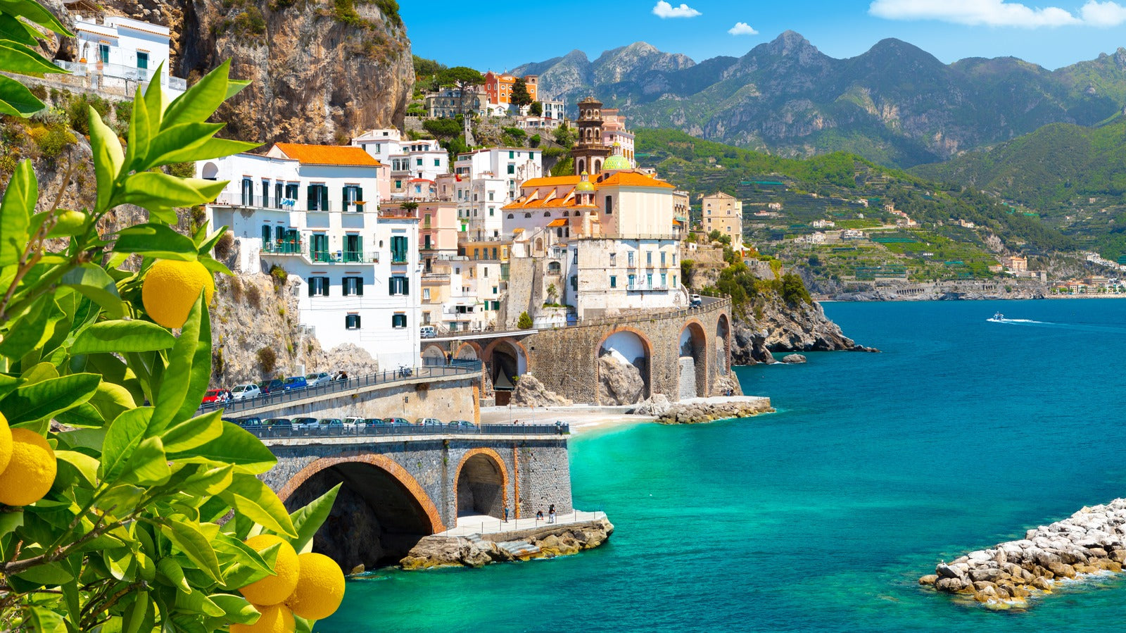 Limoncello Coast Scenic view of a coastal town with mountains and clear blue water.