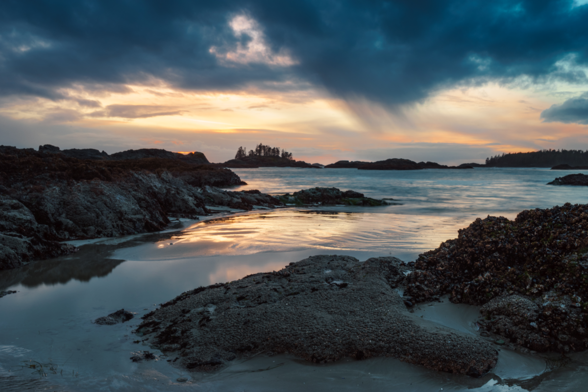 Sunset over a rocky beach with water reflecting the colors of the sky.